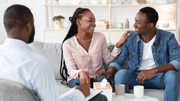 Black couple laughing while therapist watches them.